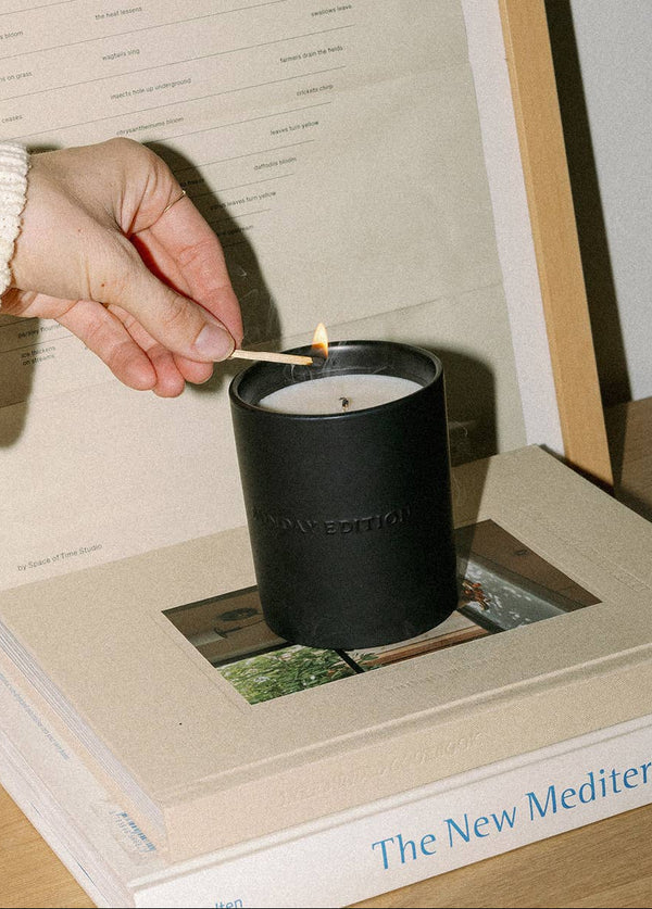 Person lighting a black candle with 'New Edition' branding on a book titled 'The New Meditator'.